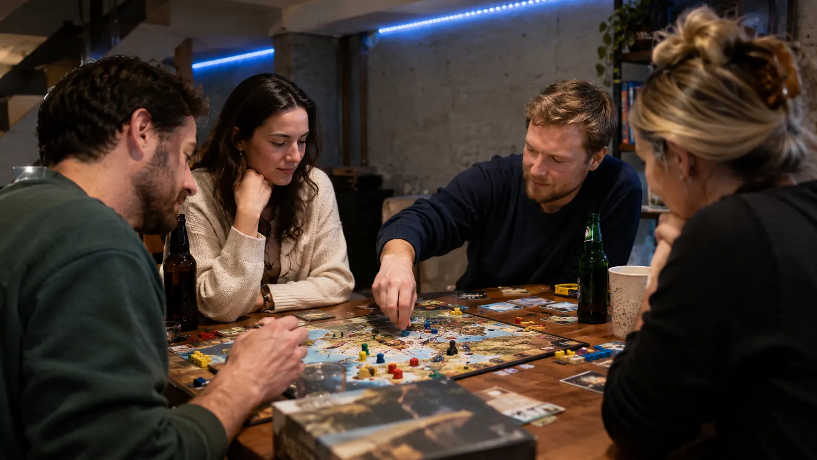 A group of adults playing board games at a table in a basement, with a softly lit LED strip in the background