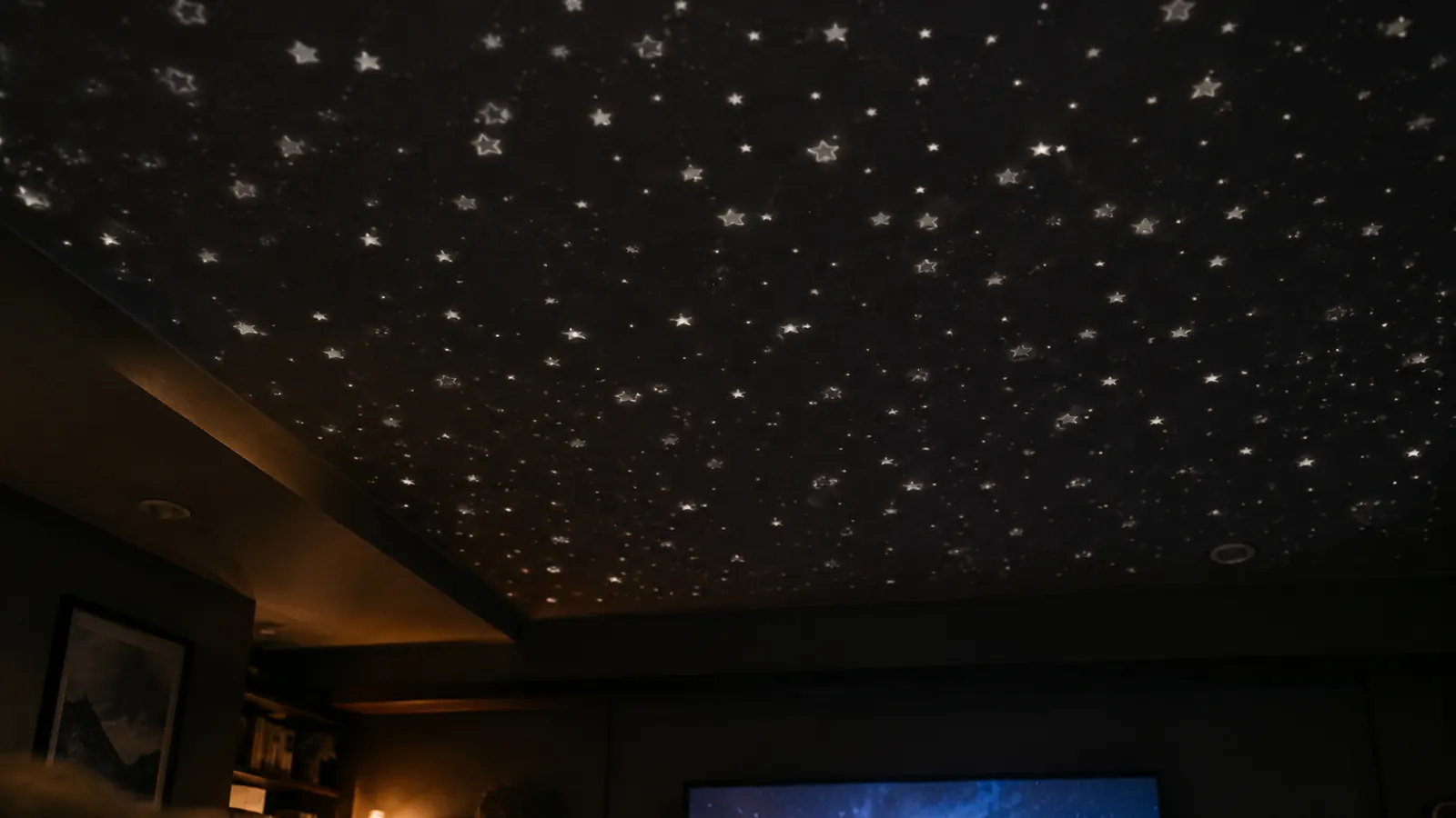 View from a couch looking up at a ceiling with a soft white starfield and the top edge of a television screen at the bottom of the frame