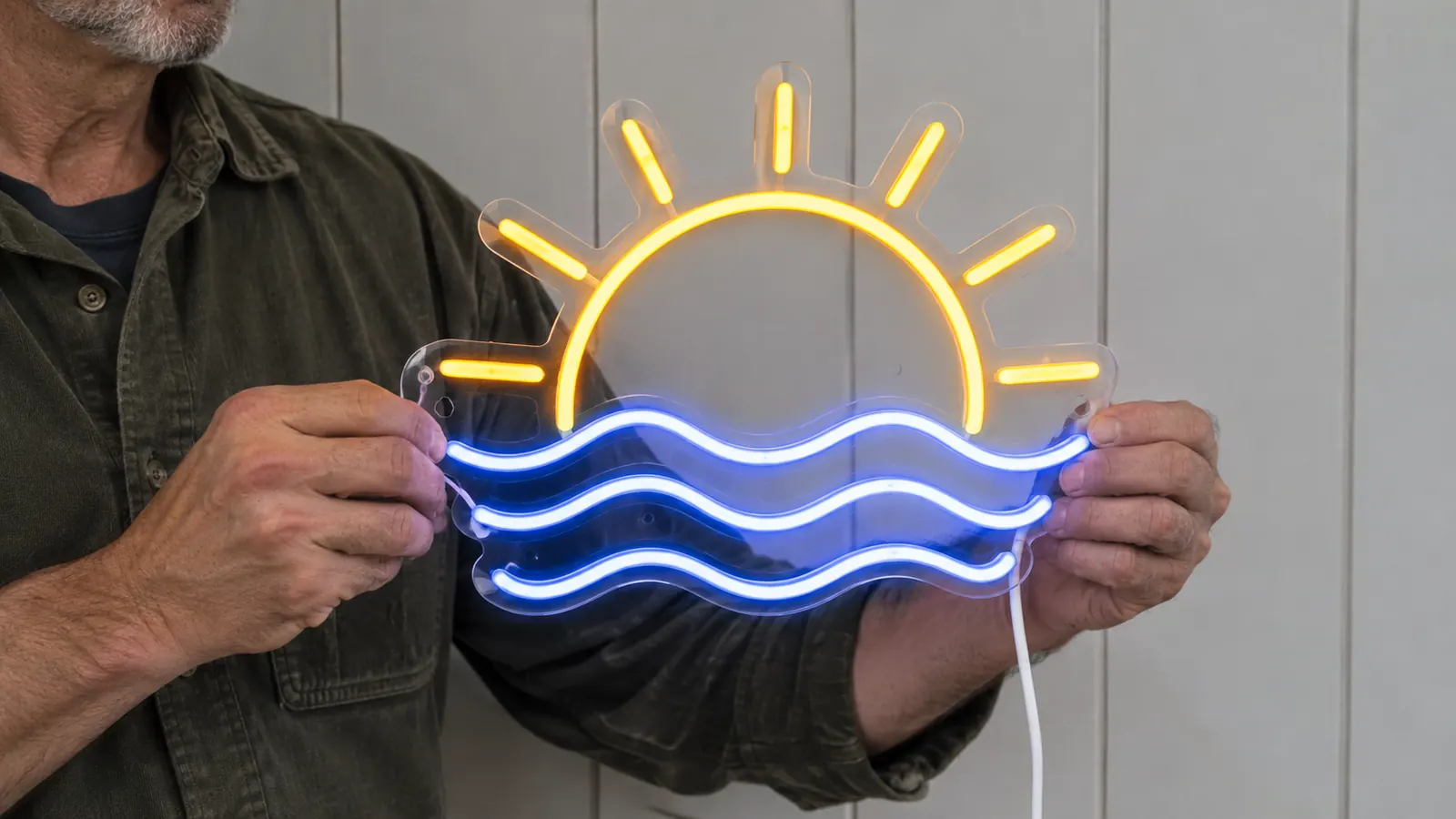 A person's hands holding a custom neon sign against a wall before mounting it